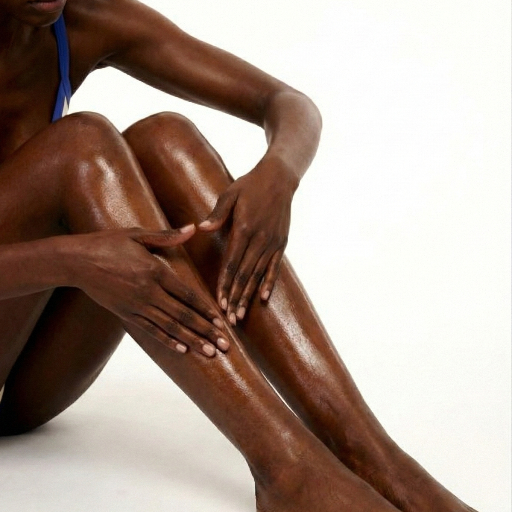 Woman sitting on a white background with her legs extended, showing her skin texture.